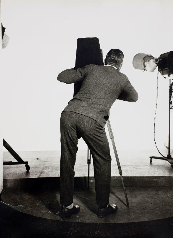 (Self Portrait? Suited man from behind with camera on tripod)
