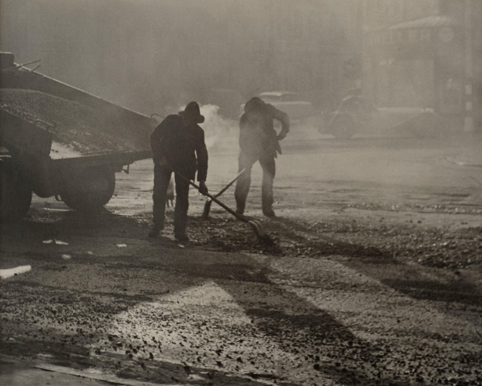 (Two men shovelling metal onto a road)